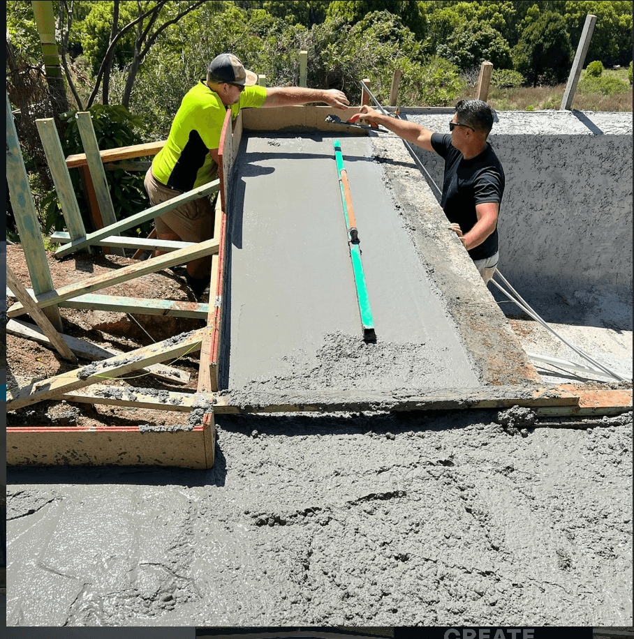 Two construction workers leveling and smoothing wet concrete for a pool edge using hand tools.